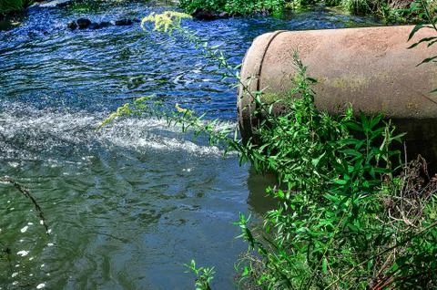 Water flows from the pipe into the river. Stock Photos