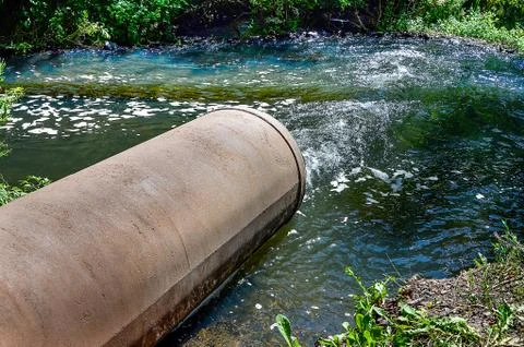 Water flows from the pipe into the river. Stock Photos