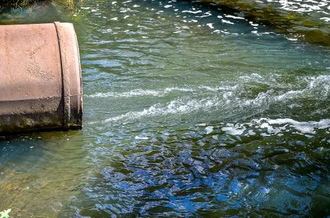 Water flows from the pipe into the river. Stock Photos