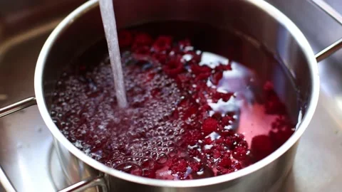 Water flows into a pot with raspberries for making compote. 4K. Stock Footage 223661603