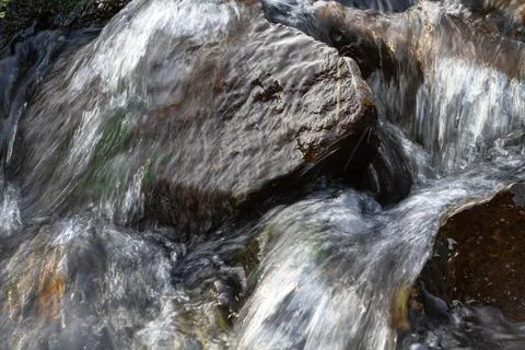 The water flows quickly between the dark stones Stock Photos