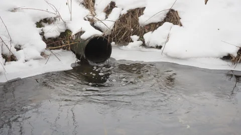 Water flows from rusty metal pipe into river during winter thaw Stock Footage 329168601