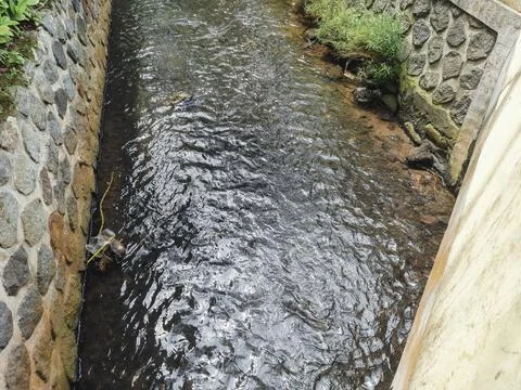 Water flows slowly through a small canal with concrete walls Stock Photos