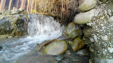 The water flows in a small canal towards a river with many rocks Video stock 243406660