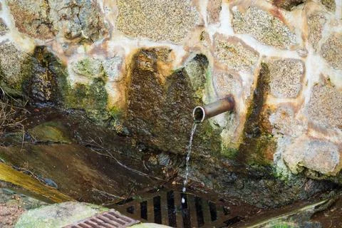 Water flows from a small pipe built into a stone wall Stock Photos