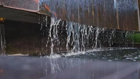 Water flows smoothly over a metal edge, creating small splashes as it tumbles 動画素材 344528056