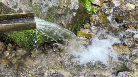 Water that flows from the spring in the mountains and descends through a gutter Stock Footage 249981995