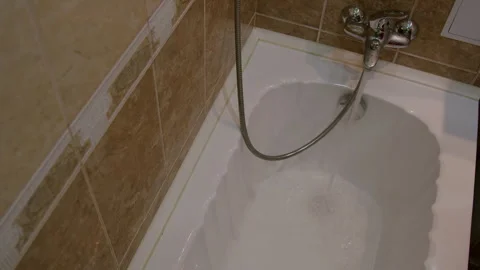 Water flows steadily from a showerhead into a white bathtub, creating ripples in Stock Footage 325482162