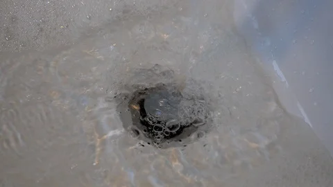 Water flows from a tap into an bath with an open plug Stock Footage 98658999