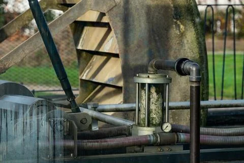 Water flows through a clear pipe connected to a water wheel at a park. Stock Photos