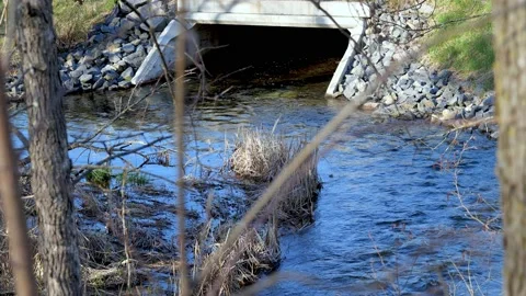 Water flows under a concrete culvert bridge beneath a road in Minnesota Stock Footage 153862124