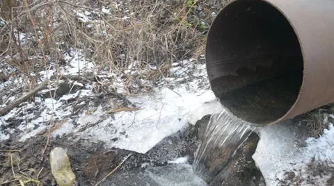 Water flows in winter from iron pipe to brook with garbage Stock Footage 50786409