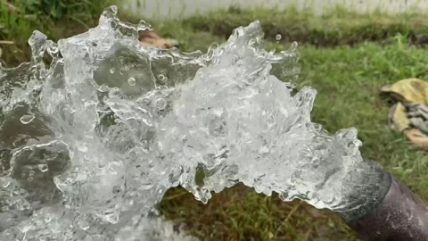 Water forcefully flows from an old metal pipe into a lush green field Stock Footage 310733804