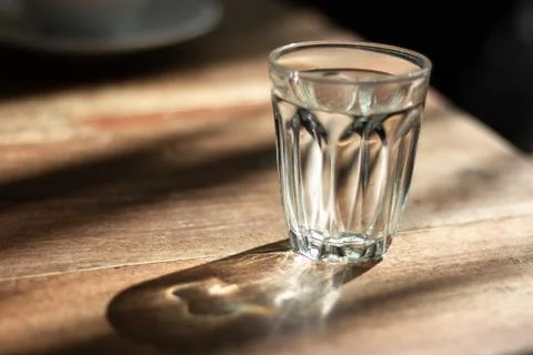 Water in glass on wooden table with shadow ,morning sunshine Photos