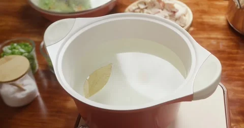Water heats in a pot while a chef adds a bay leaf during soup preparation. Close Vídeo Stock 327158131