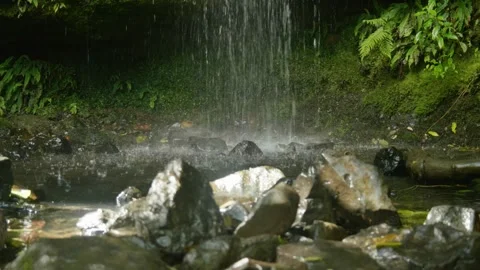 Water hitting the bottom of waterfall with light shining on rocks in front Stock Footage 260370357
