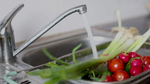 Water jet pouring flows over fresh vegetables in kitchen sink. Stock-Footage 242990839