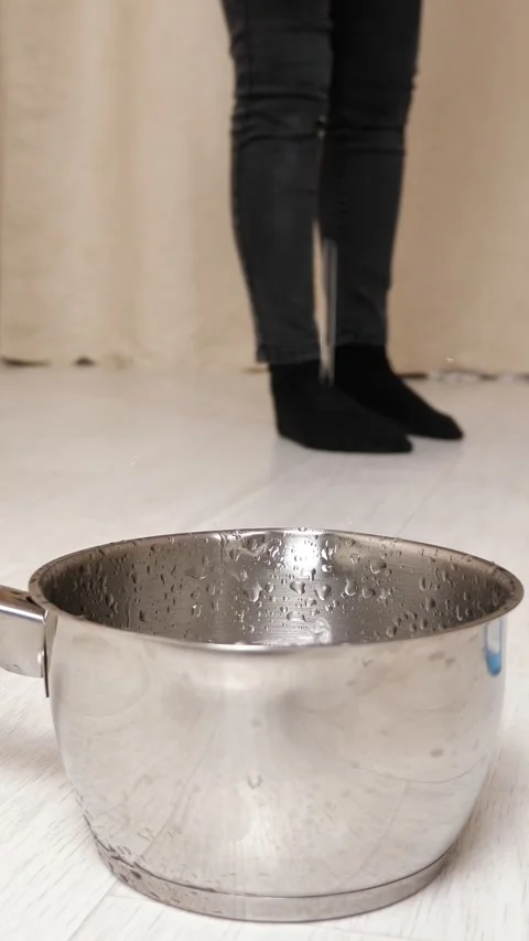 Water leaking from the ceiling into a pot while a person mops the wet floor Видео 342945585