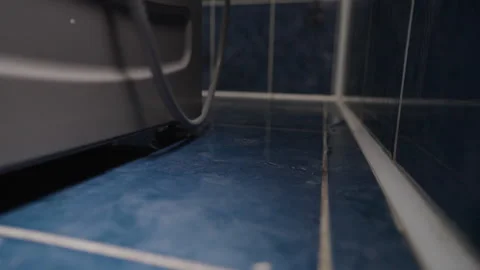 Water leaking from washing machine hose creating puddle on bathroom floor Stock Footage 313823576