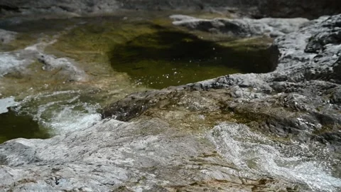 Water from a mountain river is flowing over rocks and into a pond (slow motion) Stock-Footage 212729068