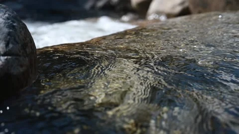Water from a mountain stream flows over rocks (slow motion) Video stock 219392300