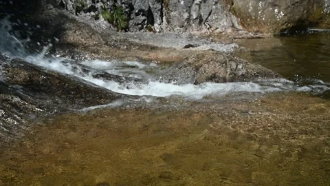 Water from a mountain stream runs over rocks and into a pool Stock Footage 219646497