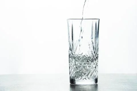 Water is poured into a crystal glass on a white background. Stock Photos