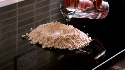 WATER IS POURED INTO A FLOUR MIXTURE TO MAKE BREAD Stock Footage