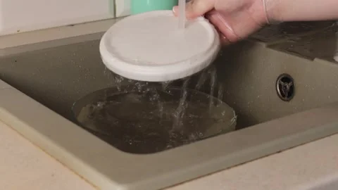 Water pouring from a faucet onto a white ceramic plate held by hand in a ki.. Stock Footage 320738341
