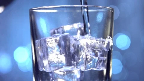 Water is pouring into a glass with ice cubes on a blue flickering background. Video stock 74640586