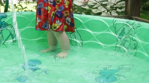 Water pours into a kiddie pool while little feet play back and forth Stock Footage 40027764