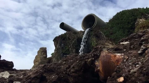 Water Pours out of drain pipe onto beach in slow motion Stock Footage 73015635