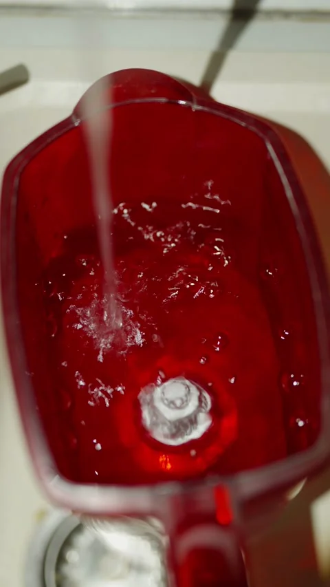 Water pours into a red transparent pitcher creating bubbles inside Stock Footage 333528408