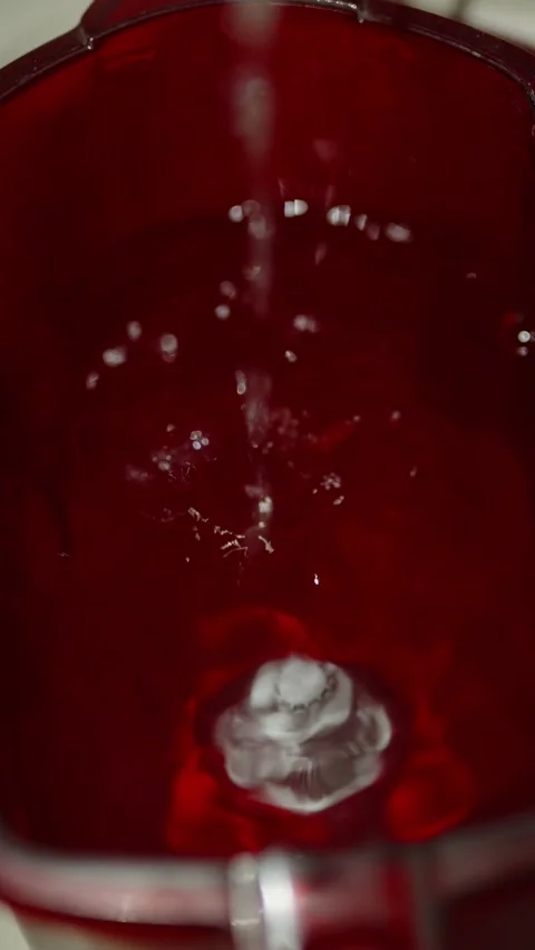 Water pours into a red transparent pitcher creating bubbles inside Stock Footage 333528450