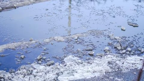 Water puddle with rocks and ice fragments reflecting blue sky and textures Stock Photos