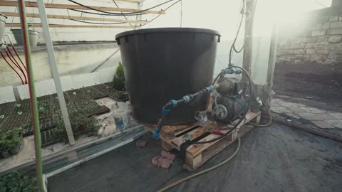 Water pump system connected to a large black tank on wooden pallets inside a Vídeo Stock 332723802