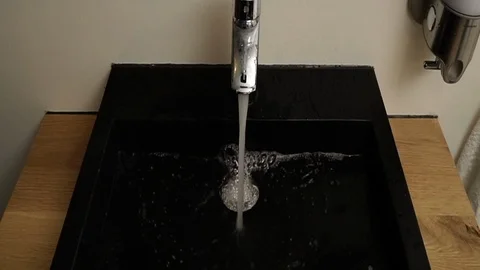 Water saving concept. Water flows from a chrome steel bathroom tap Stockbeeldmateriaal 109452852