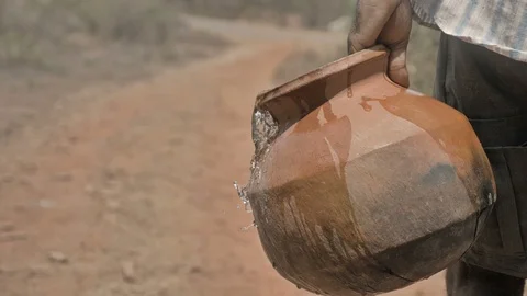 Water spilling out of an earthen pot of a farmer walking on the barren terrain Stock Footage 90098524