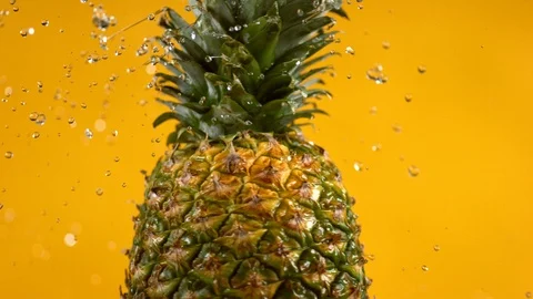Water spinning off pineapple on yellow background.  Shot in slow motion with Stock Footage 125340605