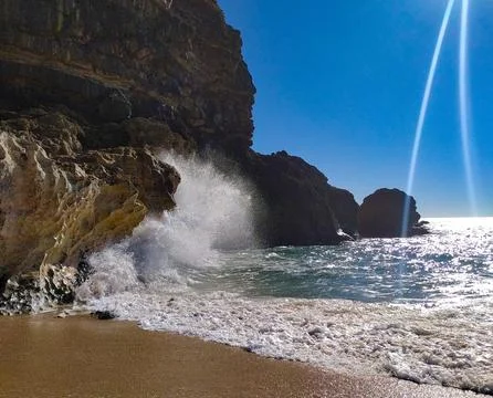 Water splashes against the rugged cliffs as waves roll in, sparkling under br Stock Photos