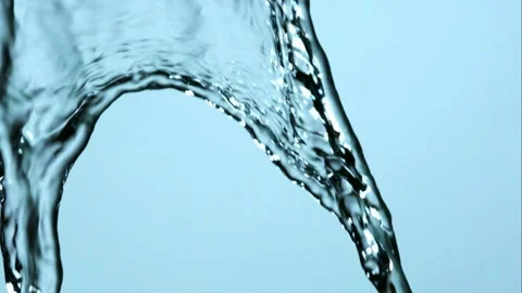 Water splashes dynamically against bright blue background Stock Footage 326753998