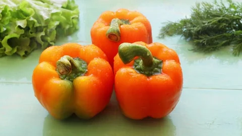 Water splashes fall on three sweet orange peppers on a green wooden background Stock Footage 237307069