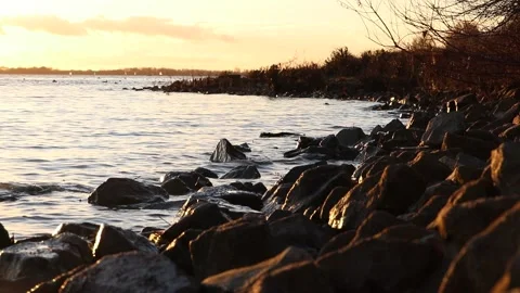 Water splashes over rocks on a sunset lake Video stock 144894091