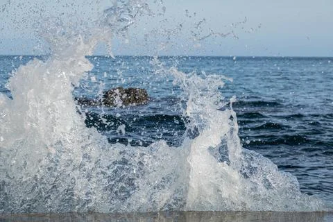 Water splashes from waves hitting rocks by the shoreline Stock Photos