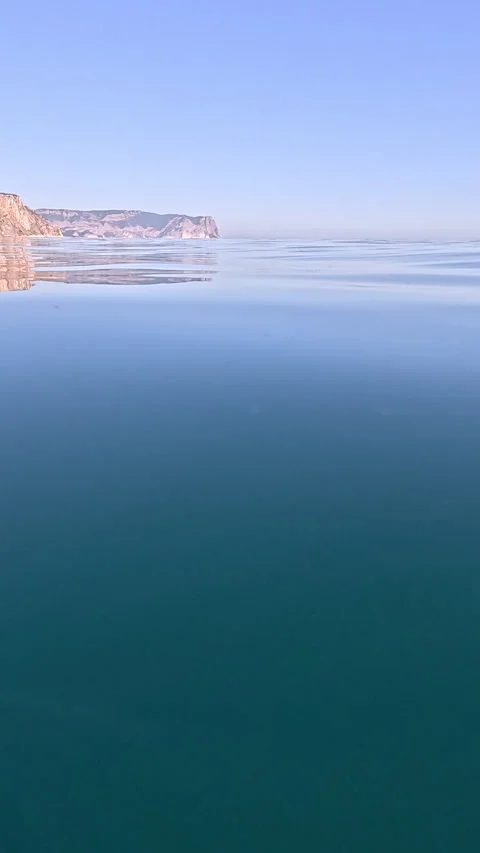 Water Split Ocean view of calm surface and deep water with distant cliffs under Stock Footage 312546601