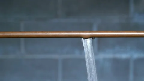 Water spraying from a thawed ruptured copper pipe against a basement wall Stock Footage