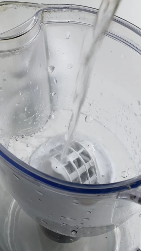 Water stream fills transparent filter jug in bright kitchen, illustrating daily Stock Footage 305772680