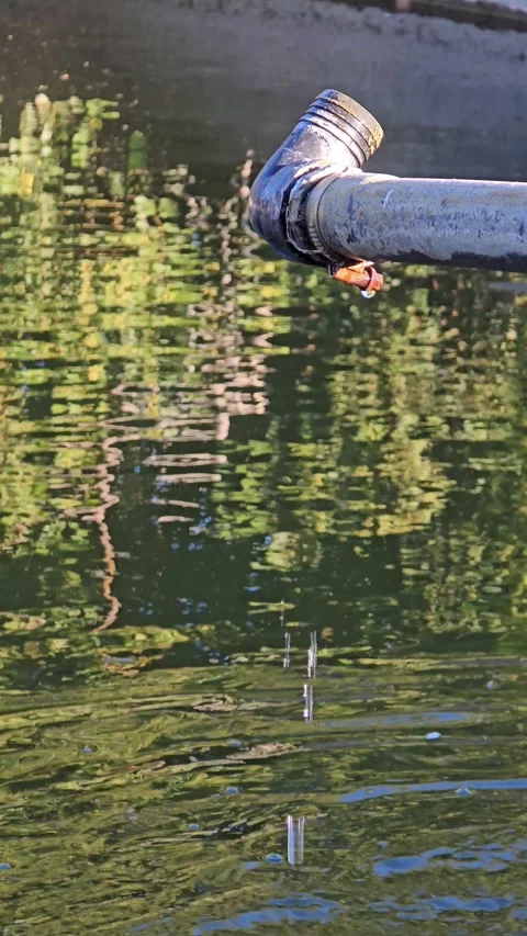 Water stream flowing from a metal pipe into a pond, generating expanding ri.. Stock Footage 314861748