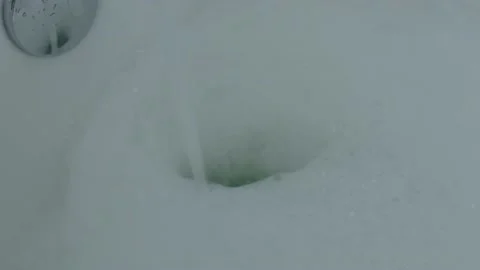 Water stream making hole in white foam soap foamy bubbles in bathtub bathroom Stock Footage 217047888