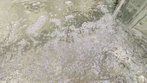 Water stream in slow motion falls on a clean surface, creating air bubbles. Stockbeeldmateriaal 170857464
